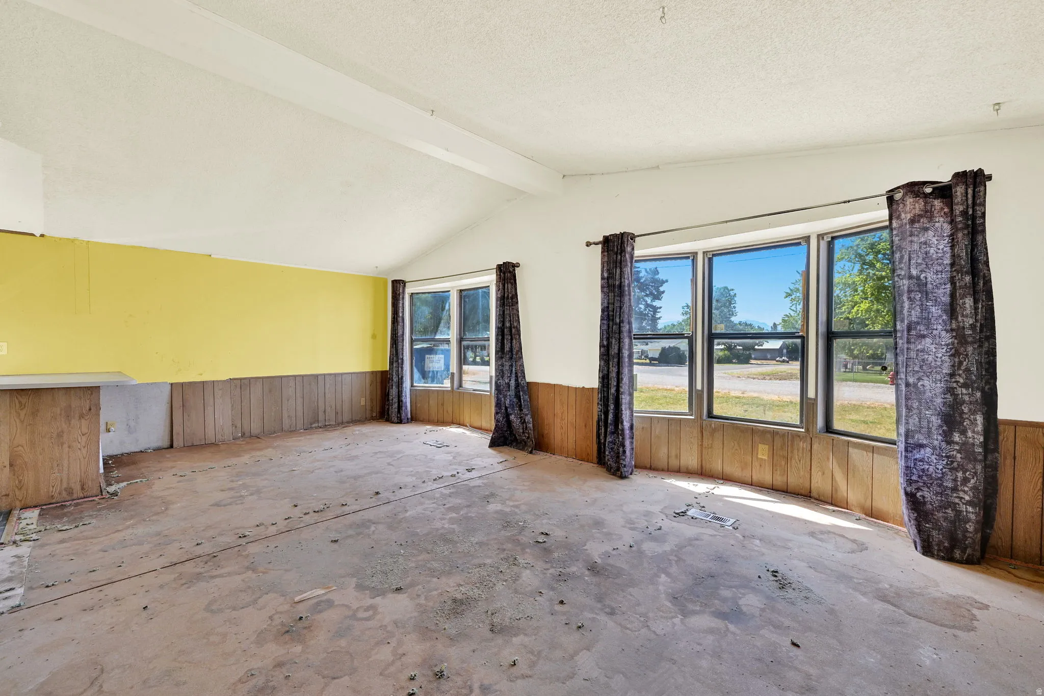 Room featuring vaulted ceilings, a bay window with three panes, wood paneling on lower walls, and a built-in counter surface