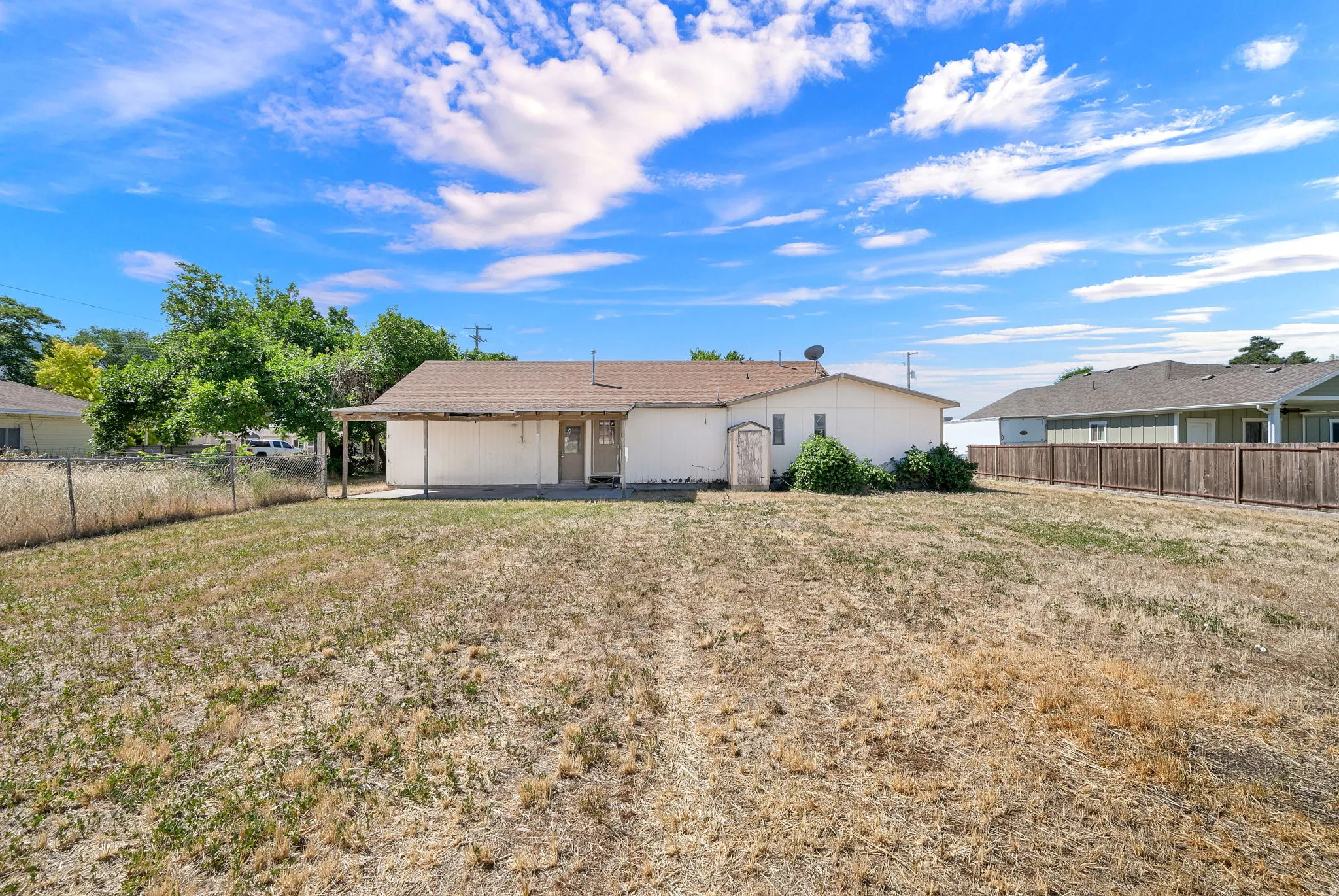 Expansive backyard featuring a covered patio, chain-link fencing, and a separate wood-panel fence