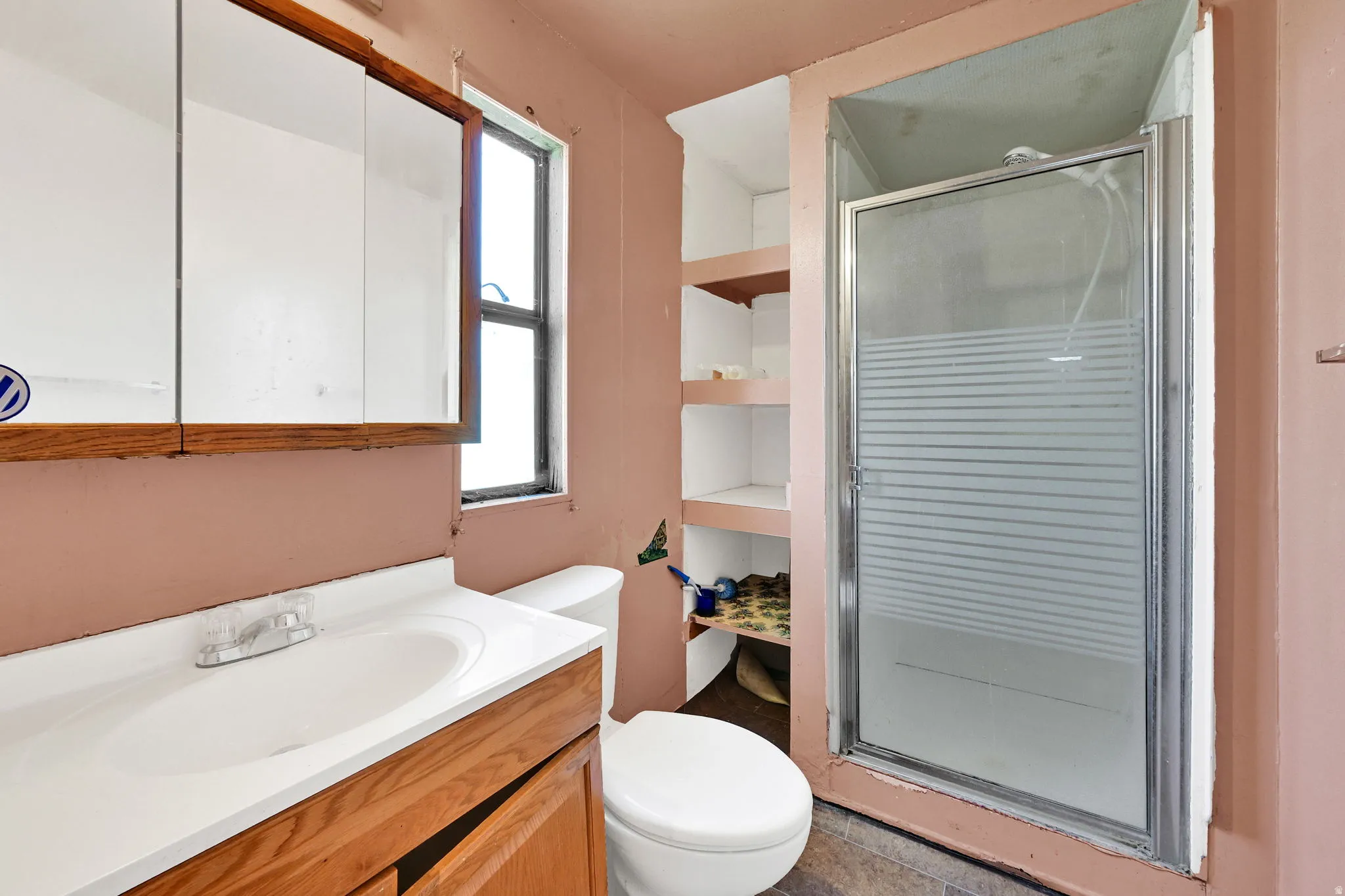 Primary suite bathroom featuring a wood-finish vanity with an integrated sink, a medicine cabinet, a window, a toilet, and a glass-enclosed shower with frosted detailing