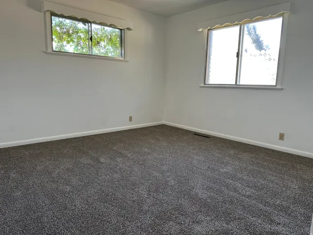 Plush gray carpeting and white painted walls with two windows featuring valances