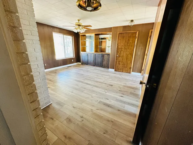 Spacious room featuring wood-finish flooring, wood paneling, a large window, and built-in cabinetry with glass display shelves