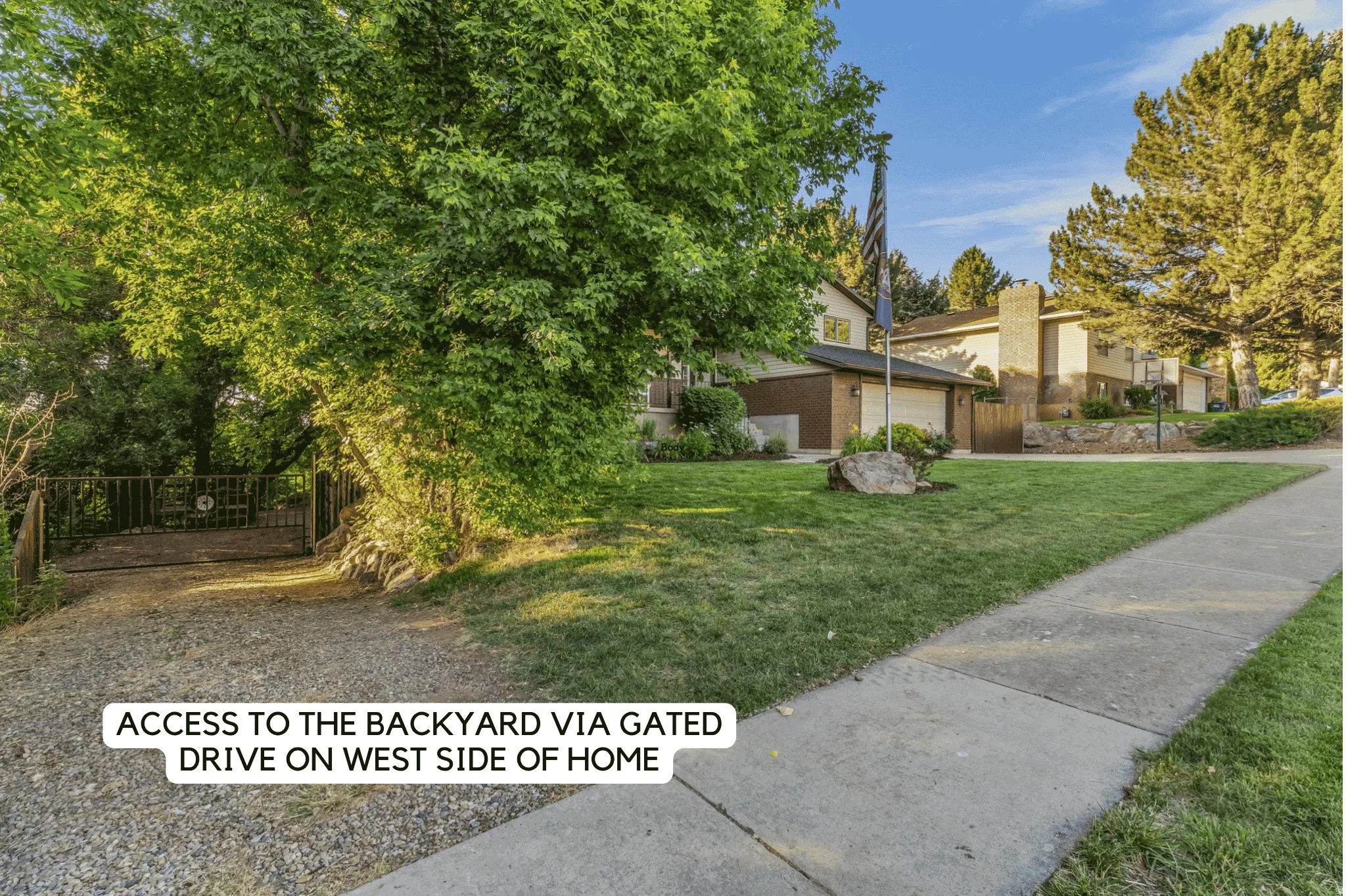 Gated drive access to the property's rear, flanked by mature trees and a manicured lawn