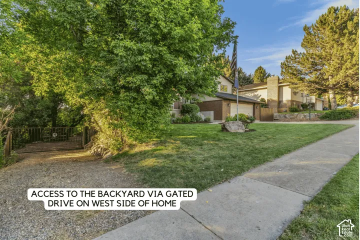 Gated drive access to the property's rear, flanked by mature trees and a manicured lawn