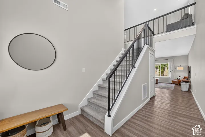 Two-story entryway featuring wood-finish flooring, a carpeted staircase with black iron railings, and a prominent second-story landing overlooking the space
