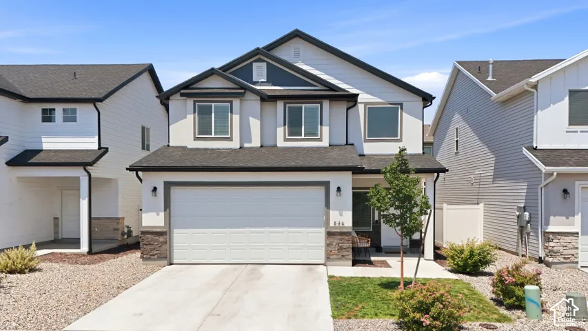 Contemporary two-story residence featuring a two-car garage, dark shingle roof, and stucco exterior with stone veneer accents