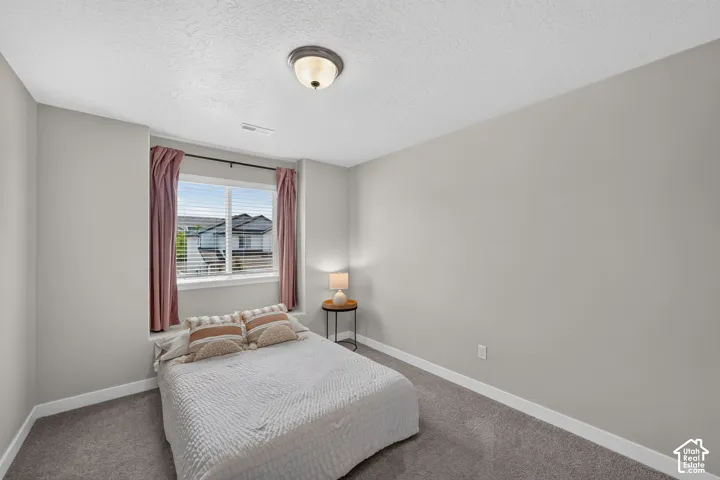 Bedroom featuring a window with blinds, a ceiling-mounted light fixture, light gray walls, white trim, and gray carpet flooring
