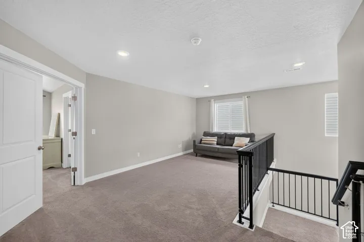Open loft space featuring neutral carpeting, light gray walls, recessed lighting, and white trim