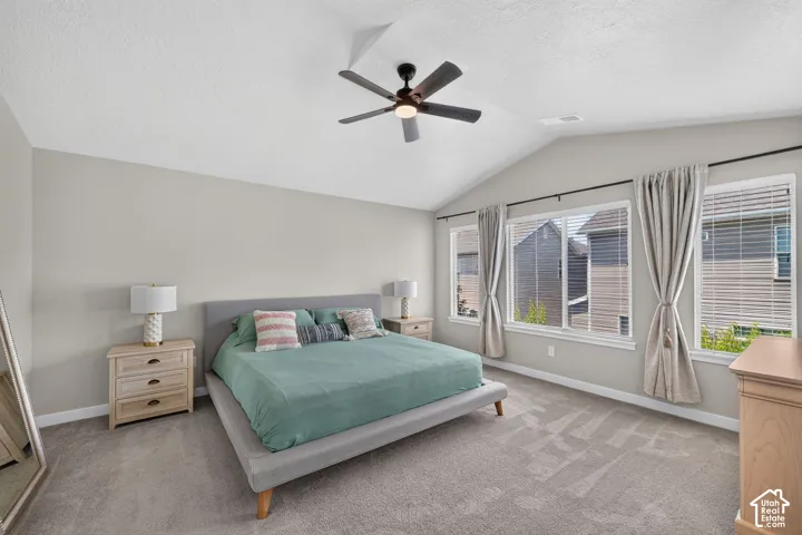 Vaulted ceiling bedroom featuring plush gray carpeting and a modern ceiling fan