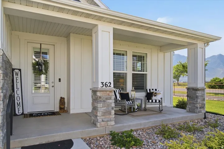 Covered front porch featuring white board and batten siding and stone column accents