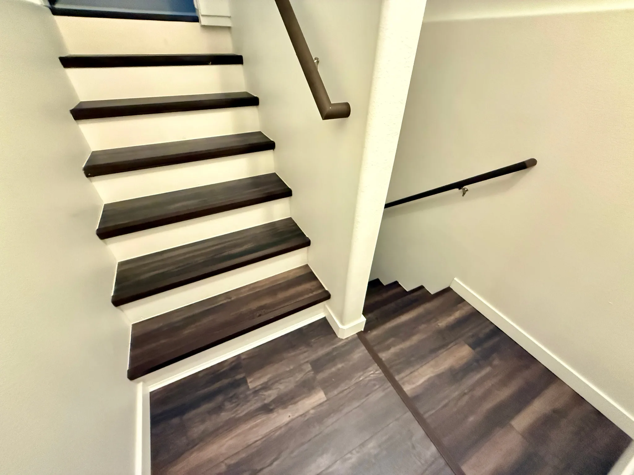 Multi-level staircase featuring dark wood-finish treads and risers, coordinating wood-finish flooring, and a dark-toned handrail