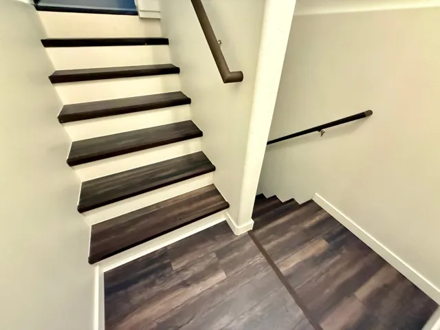 Multi-level staircase featuring dark wood-finish treads and risers, coordinating wood-finish flooring, and a dark-toned handrail
