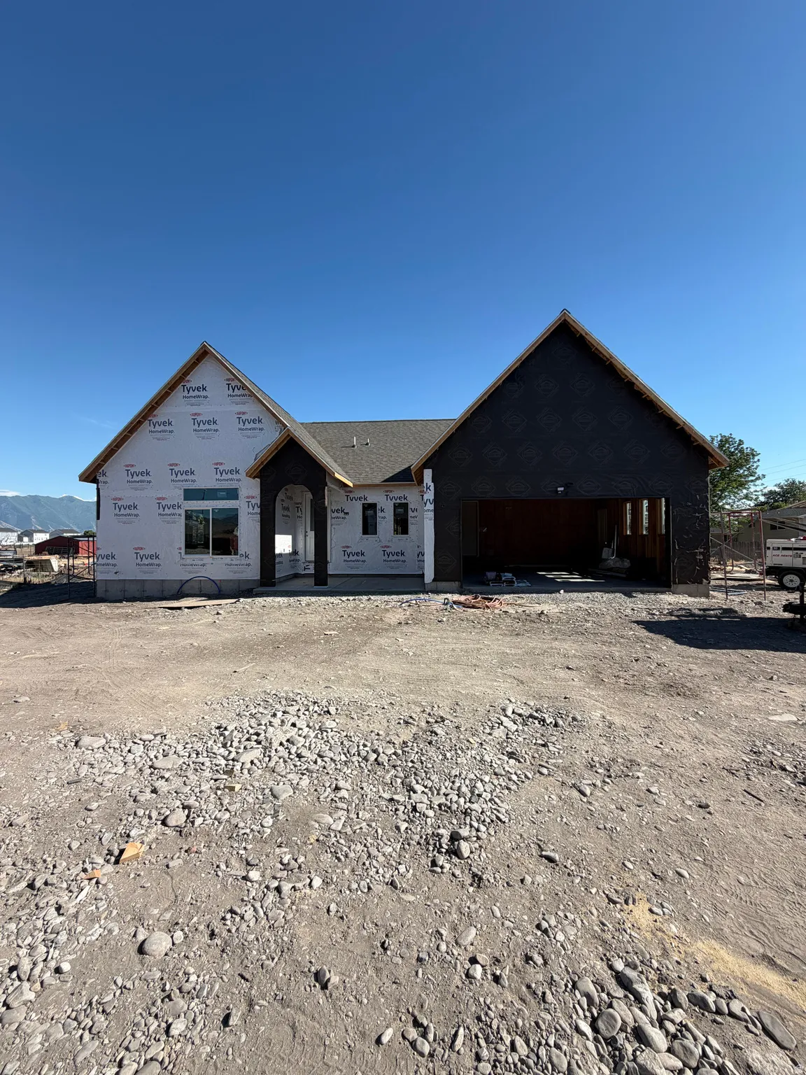 Single-story residential structure under construction featuring a prominent arched entry, dual gabled rooflines, and an integrated three-car garage
