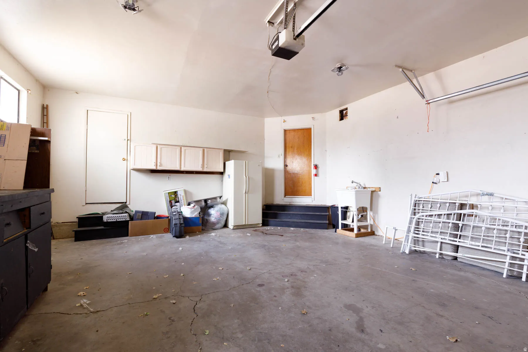 Spacious garage featuring a concrete floor, overhead garage door opener, multiple windows, built-in cabinetry, and a utility sink