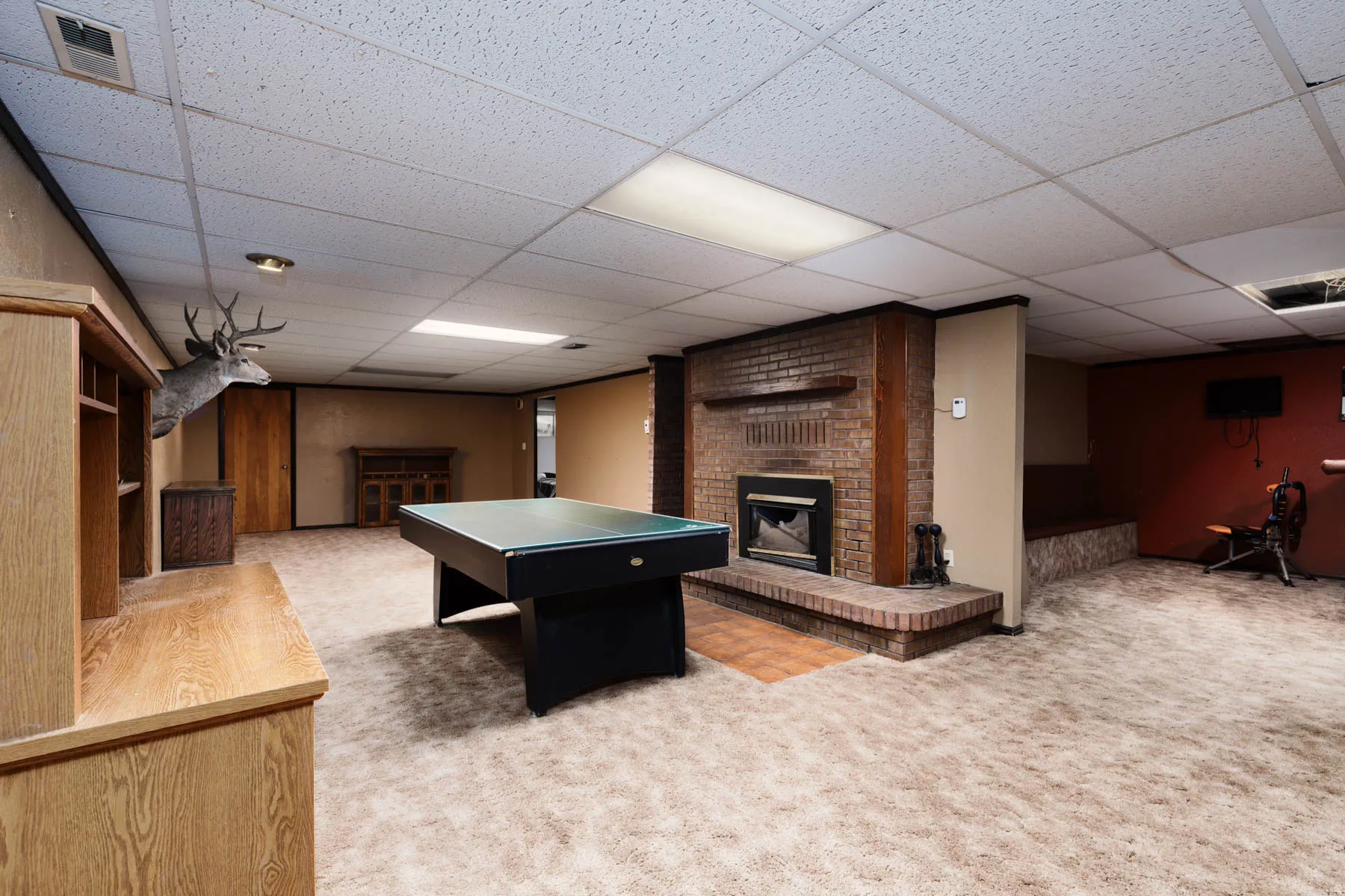 Spacious lower level featuring a brick fireplace, built-in shelving, carpet flooring, and recessed lighting