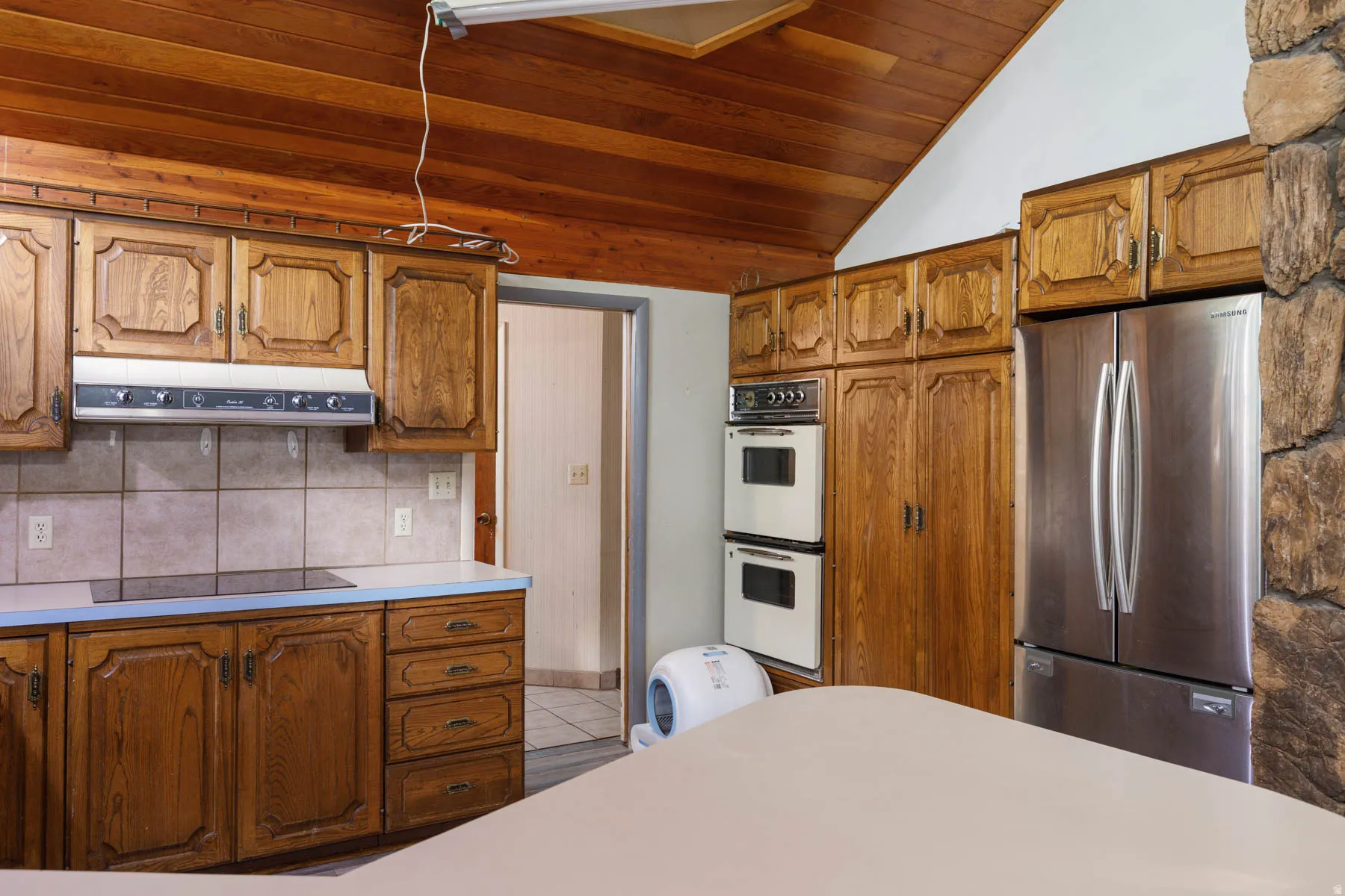 Kitchen featuring wood cabinetry, stainless steel refrigerator, double wall ovens, cooktop, and a tile backsplash