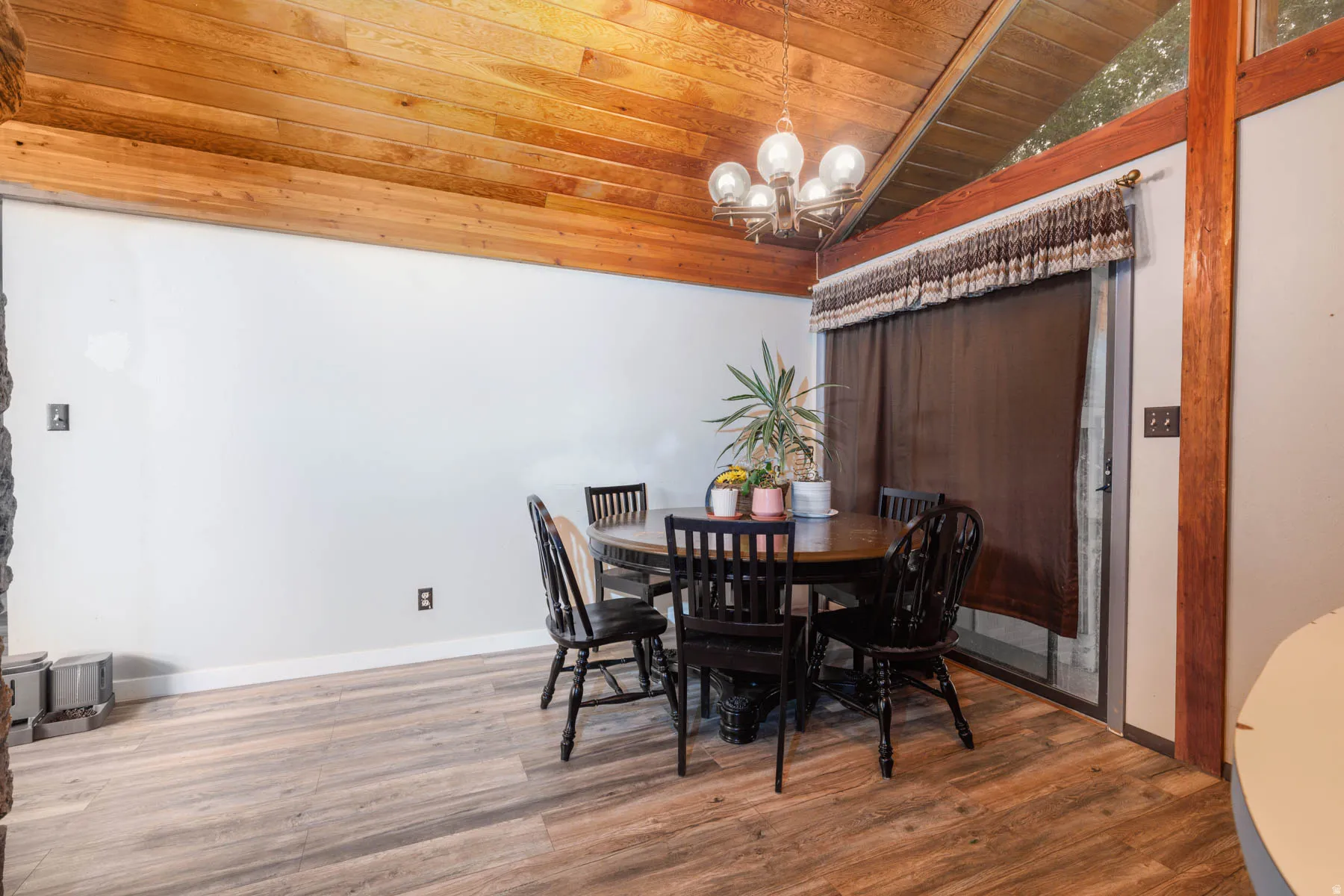Wood-finish flooring with a vaulted wood plank ceiling, a built-in stone element, a glass sliding door, and an overhead chandelier
