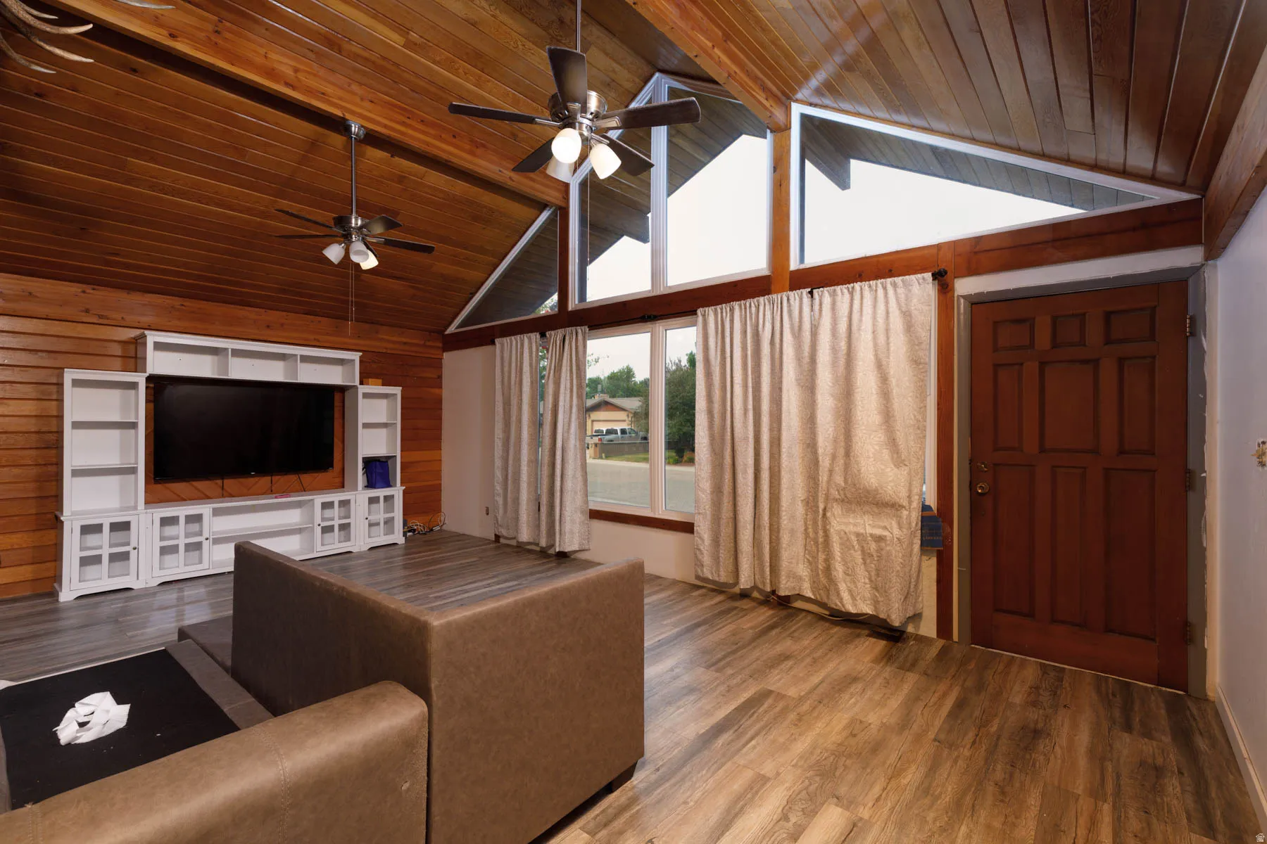 Vaulted wood-paneled ceilings with exposed beams, wood-finish flooring, built-in entertainment center, and expansive upper windows