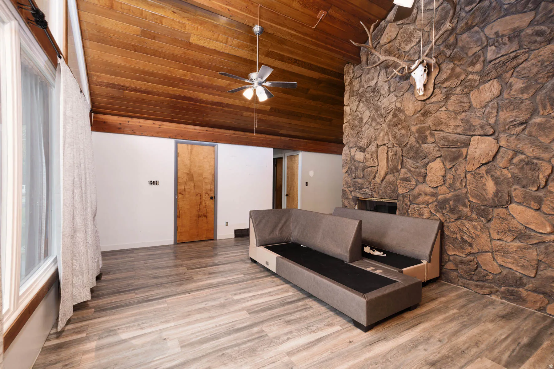 Spacious interior featuring a vaulted wood-paneled ceiling, a substantial stone fireplace, wood-finish flooring, and a ceiling fan with integrated lighting