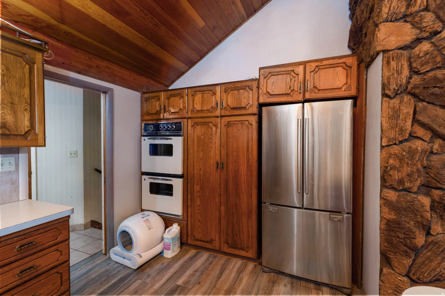 Kitchen featuring wood-finish cabinetry, integrated double wall ovens, a stainless steel French door refrigerator, and a stone accent wall
