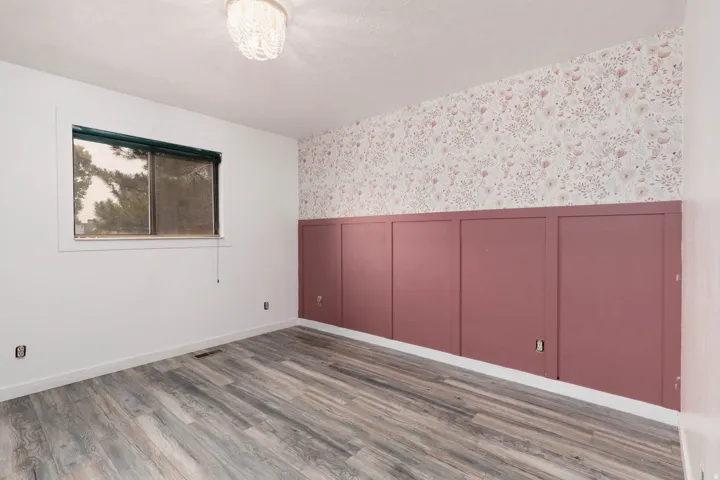 Interior room featuring wood-finish flooring, a window, and a decorative wall with wainscoting and floral wallpaper