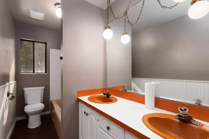 Bathroom vanity featuring dual orange sinks and white cabinetry, complemented by a large wall-mounted mirror