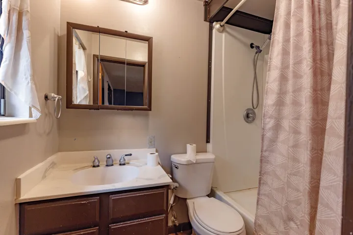Bathroom featuring a single vanity with a white countertop and wood-finish cabinetry, a shower with a showerhead, and a wall-mounted mirror