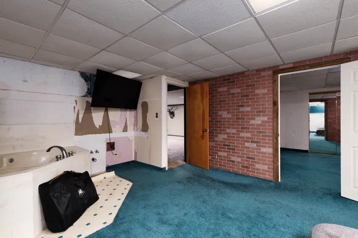 Room featuring a built-in jetted tub, brick accent wall, and drop ceiling with integrated lighting