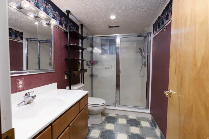 Bathroom featuring a single-sink vanity with wood-finish cabinetry, a framed mirror with overhead lighting, a shower enclosure with a glass door, and geometric pattern flooring