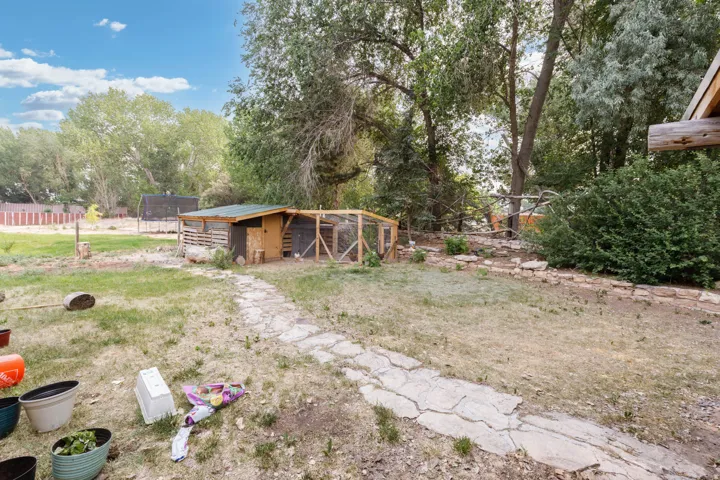 Expansive rear yard featuring a stone pathway, mature trees, and a functional outbuilding with an attached fenced enclosure