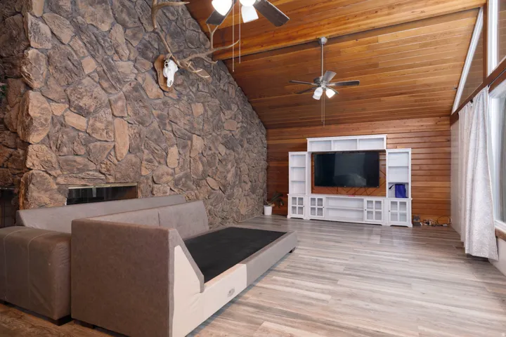 Spacious living area featuring a vaulted wood-paneled ceiling, a stone accent wall, and wood-finish flooring
