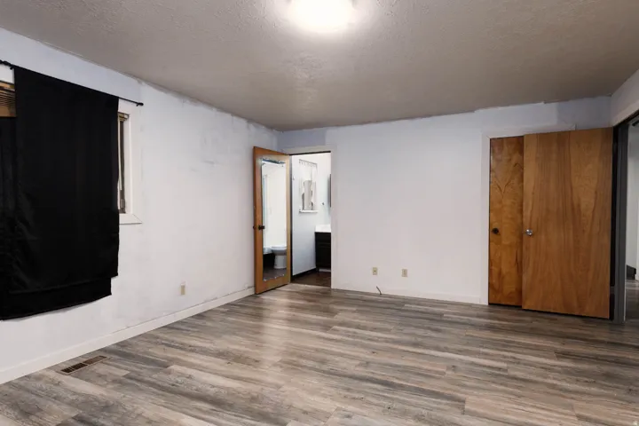 Spacious room featuring wood-finish flooring, white walls, and a window with a dark curtain