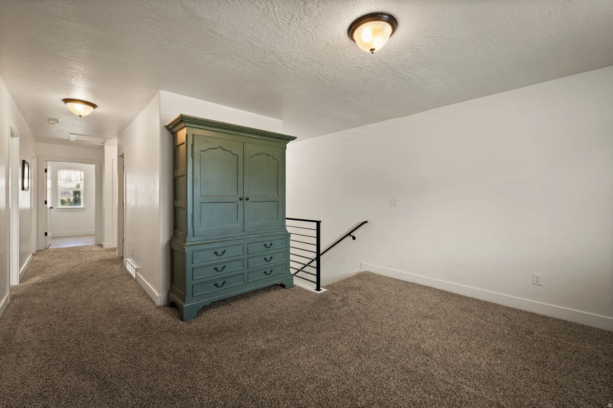 Carpeted hallway with a window at its end, featuring white walls and baseboards
