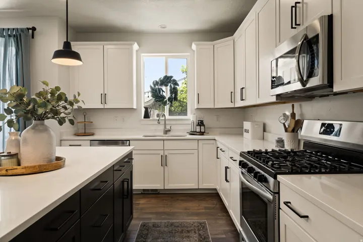 Gourmet kitchen featuring white shaker cabinetry, stainless steel appliances, a center island with contrasting black cabinetry, white countertops, and wood-finish flooring