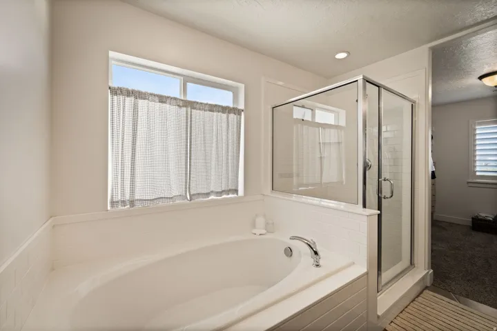 Soaking tub with a polished chrome faucet, surrounded by white subway tile, a glass-enclosed shower, and a recessed ceiling light