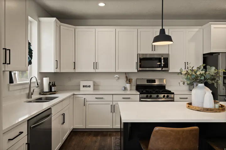Modern kitchen featuring white shaker cabinetry, stainless steel appliances including a gas range and microwave, light-toned countertops, and dark wood-finish flooring