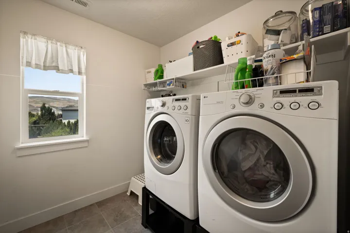 Dedicated laundry space featuring a side-by-side washer and dryer, tile flooring, and wall-mounted shelving for storage