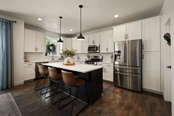 Contemporary kitchen featuring a large central island with seating, white shaker cabinetry, stainless steel appliances, and wood-finish flooring
