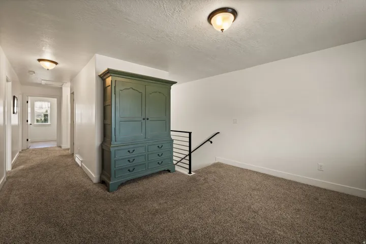 Carpeted hallway with a window at its end, featuring white walls and baseboards