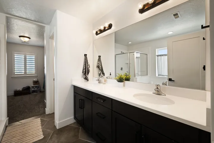 Bathroom featuring a dual vanity with dark cabinetry and a white countertop, a large mirror, and overhead vanity lighting