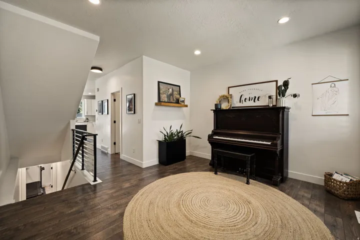 Wood-finish flooring throughout the main level featuring recessed lighting, white baseboards, and a contemporary metal railing system along the staircase