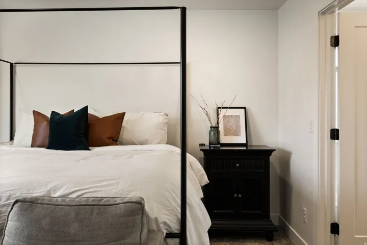 Bright bedroom featuring a dark metal four-poster bed frame, white walls, and carpet flooring