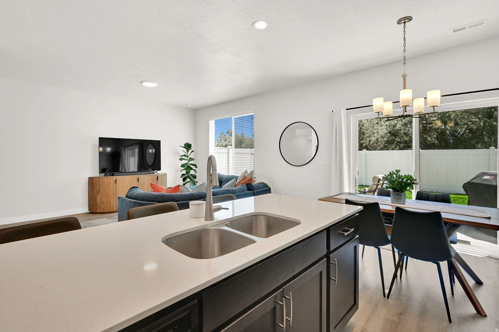 Open-concept living space featuring a kitchen island with dual stainless steel sinks, dark cabinetry, and light-toned countertops