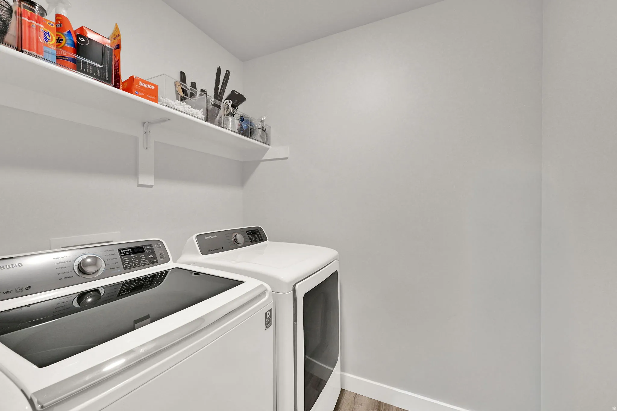 Dedicated laundry area featuring white walls and wood-finish flooring