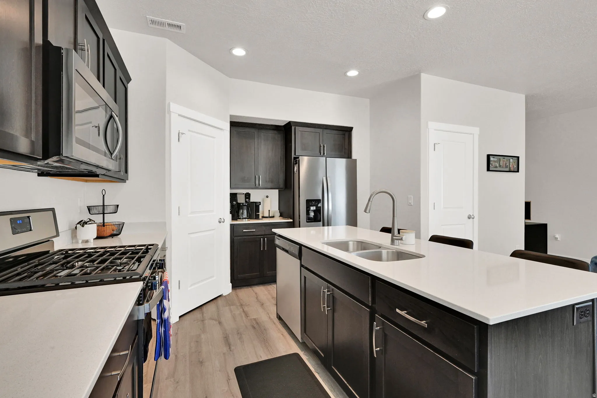 Modern kitchen featuring dark wood-finish cabinetry, stainless steel appliances, and light-toned countertops