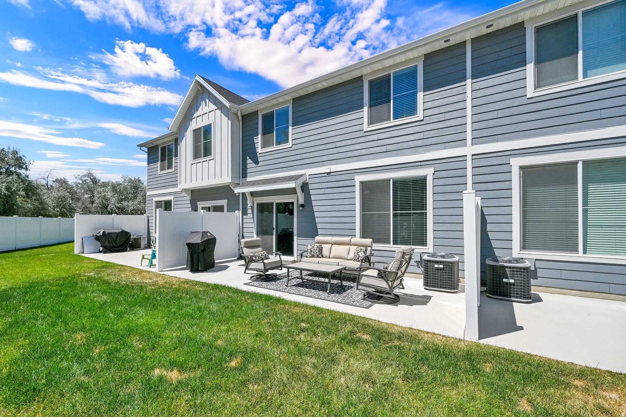 Rear exterior featuring a concrete patio, sliding glass door access, white privacy fencing, and two exterior HVAC units