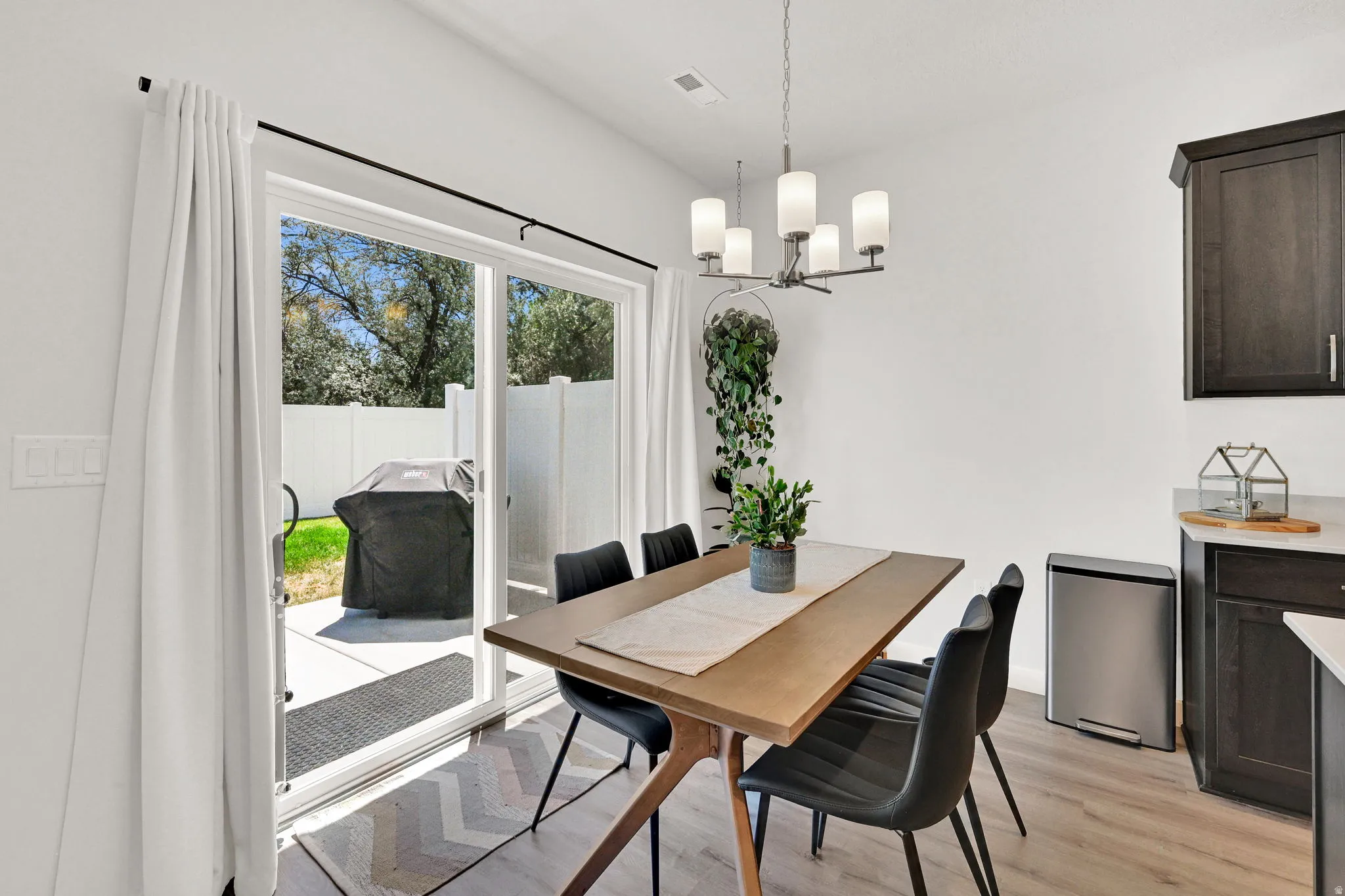 Dining area featuring wood-finish flooring, a contemporary chandelier, and a sliding glass door providing direct access to the concrete patio