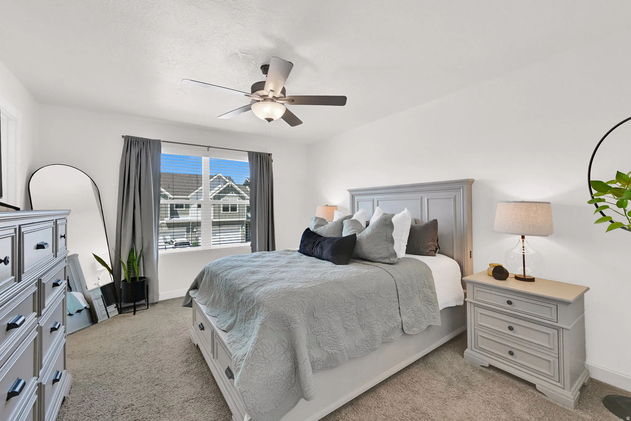 Carpeted room featuring a ceiling fan with integrated lighting, a large window with blinds and drapes, and a paneled headboard