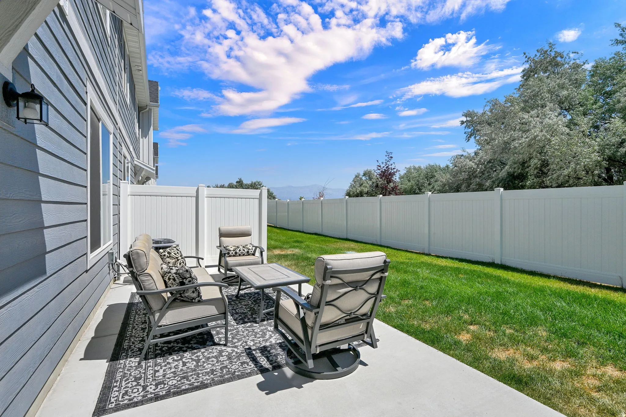 Concrete patio featuring a privacy fence, manicured lawn, and exterior siding