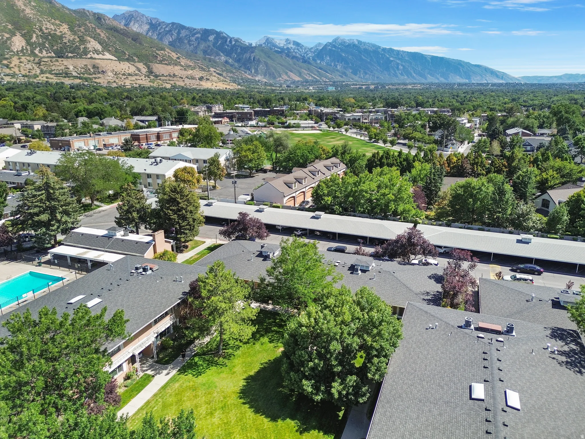Community featuring multiple buildings with dark shingle roofs, surrounded by mature trees and manicured green spaces