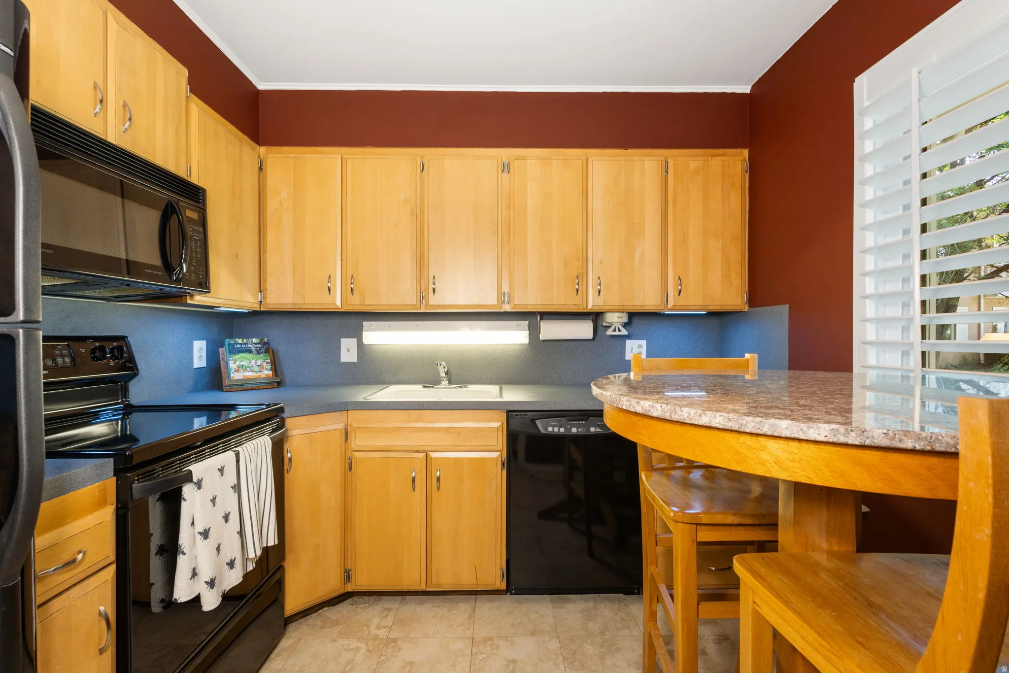 Kitchen featuring light wood cabinetry, black appliances, solid surface countertops, and a built-in breakfast bar